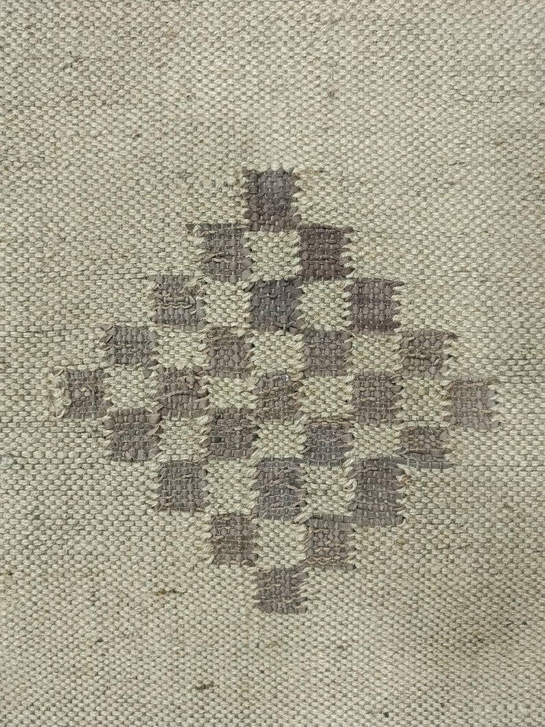 May include: A close-up of a woven rug with a diamond-shaped pattern in shades of brown and beige.