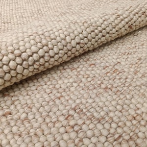 Puede incluir: Primer plano de una alfombra de lana de color crema con una superficie texturizada y abultada. La alfombra está hecha de pequeñas bolas redondas de lana que están estrechamente tejidas.