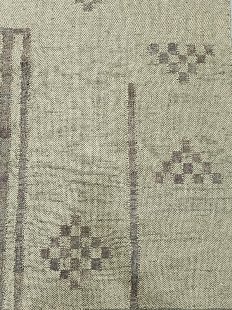 May include: A close-up of a beige rug with a woven pattern. The rug has a subtle geometric design in a darker shade of beige.