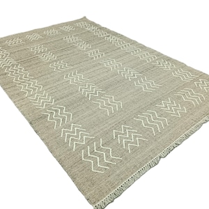 Peut inclure: Un tapis gris et blanc avec un motif géométrique. Le tapis a une bordure frangée.