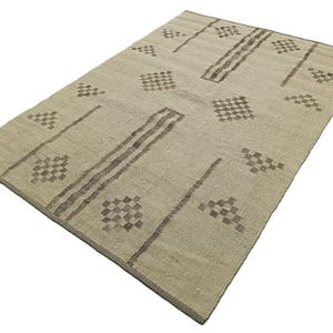 May include: A beige rug with a geometric pattern in brown. The pattern features rows of small squares and diamonds.