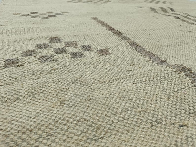May include: A close-up of a woven rug with a subtle geometric pattern in a light beige color.