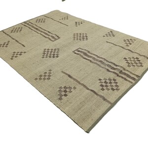 May include: A beige rug with a geometric pattern in brown. The pattern features squares and diamonds.