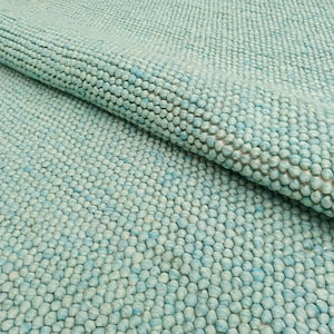 Puede incluir: Primer plano de una alfombra azul claro texturizada hecha de pequeñas bolas redondas de hilo. La alfombra tiene una textura suave y peluda.