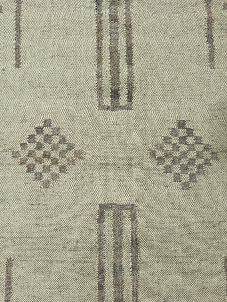 May include: A beige rug with a geometric pattern in brown. The pattern includes vertical stripes and diamond shapes.