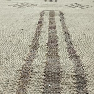 May include: Close-up of a woven rug with a light beige background and two dark brown stripes running down the center.