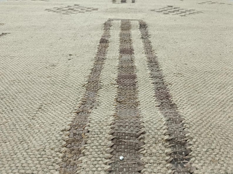 May include: Close-up of a woven rug with a light beige background and two dark brown stripes running down the center.