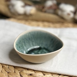 May include: A small, triangular ceramic bowl with a white exterior and a green and blue glaze. The bowl has a speckled, textured finish.