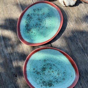 Peut inclure: Deux assiettes ovales en céramique avec un glaçage turquoise et un bord rouge. Les assiettes ont un motif moucheté.