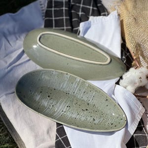 May include: Two green ceramic serving dishes in an oval shape. The dishes have a speckled glaze and a slightly textured surface.