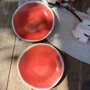 May include: Two red ceramic plates with a white rim. The plates are on a wooden surface.