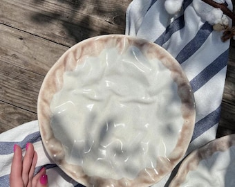 May include: Two white ceramic plates with a textured, rippled surface and a brown rim. The plates are on a blue and white striped fabric.