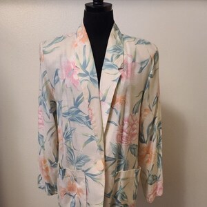 May include: A cream-colored blazer with a floral print featuring pink, orange, and green flowers. The blazer has a button closure and two pockets.