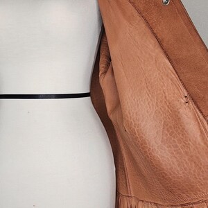 May include: A brown leather jacket with fringe detailing along the bottom hem. The jacket is displayed on a mannequin, showcasing its texture and design. The jacket has a button closure and a soft interior.