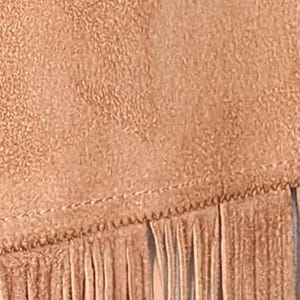 May include: Close-up of a tan suede fabric with a textured surface and a fringe detail. The fringe is made of long, thin strips of the same material, adding a decorative element to the design.