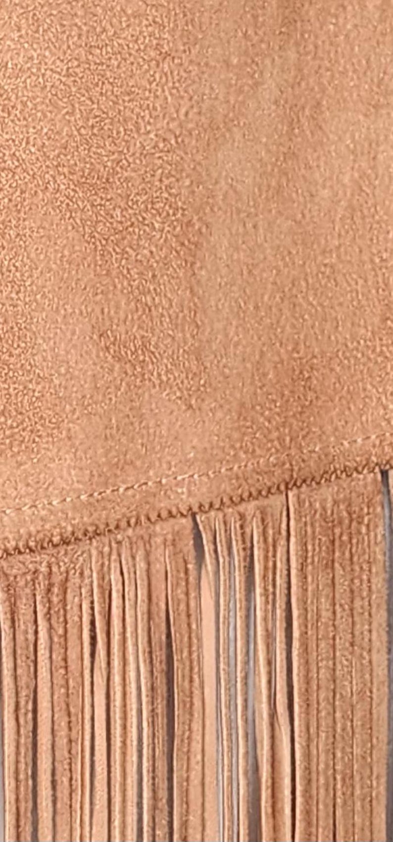 May include: Close-up of a tan suede fabric with a textured surface and a fringe detail. The fringe is made of long, thin strips of the same material, adding a decorative element to the design.