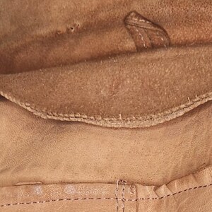 May include: Close-up of a tan leather jacket collar and lapel. The collar is folded over, revealing a soft, suede-like interior. Visible stitching and a small leather tab add detail to the design.