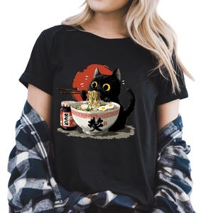 Woman wearing a T-shirt with a cute cartoon black cat eating ramen with chopsticks in front of a red sun background and soy sauce bottle.