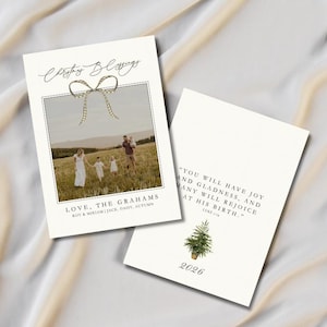 Könnte beinhalten: Zwei rechteckige Weihnachtskarten mit weißem Hintergrund. Die erste Karte zeigt ein Familienfoto auf einem Feld, eine goldene Schleifengrafik und den Text Christmas Blessings, Love, The Grahams, Roy & Miriam, Jack, Daisy, Autumn. Die zweite Karte zeigt einen kleinen Tannenbaum, das Jahr 2026 und einen Bibelvers.