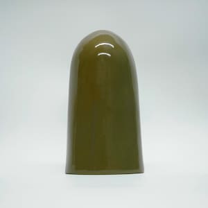 May include: A tall, olive-green ceramic object with a rounded top and a smooth, glossy finish. The shape is reminiscent of a bell or a rounded pillar. The object stands on a white surface.