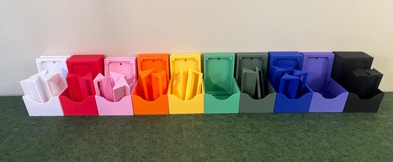 May include: A row of 12 small, open storage boxes in various colors, including white, red, pink, orange, yellow, green, gray, blue, purple, and black. Each box has a small, rectangular opening on the front.
