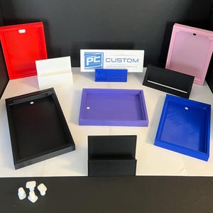May include: Assortment of acrylic display stands in various colors, including black, white, red, pink, purple, and blue. The stands are designed to hold business cards, photos, or other small items. The stands are made of clear acrylic and have a modern, minimalist design. The stands are also available in a variety of sizes to accommodate different needs.