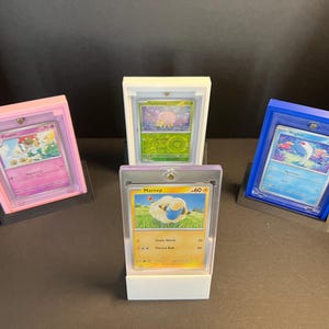May include: Four Pokemon trading cards displayed in clear plastic card holders on white, pink, and blue bases. The cards feature the Pokemon Mareep, Wigglytuff, and Flareon.
