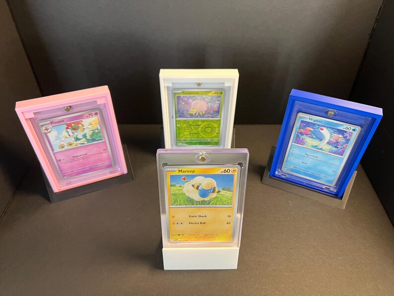May include: Four Pokemon trading cards displayed in clear plastic card holders on white, pink, and blue bases. The cards feature the Pokemon Mareep, Wigglytuff, and Flareon.