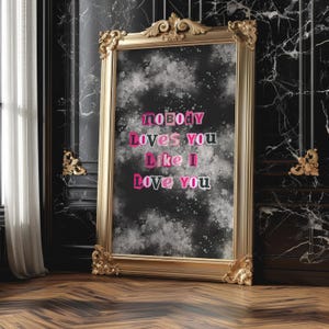 Può includere: Uno specchio con cornice dorata, sfondo nero e schizzi di vernice bianca. Lo specchio ha il testo "nobody loves you like I love you" in lettere rosa e nere.