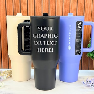 May include: Three insulated travel mugs in cream, black, and periwinkle. The black mug has the text "YOUR GRAPHIC OR TEXT HERE!" in white. Each mug has a handle and a lid. The periwinkle mug has the HydroJug logo.