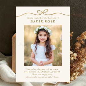 May include: Baptism invitation featuring a photo of a young girl wearing a floral crown and white dress. The invitation includes the text "You're invited to the baptism of SADIE ROSE" and event details in gold lettering.