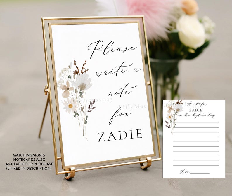 May include: A white sign with a gold frame and easel, featuring a floral design and the text "Please write a note for Zadie". A matching white card with a floral design and lines for writing a note is also included.