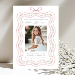 May include: A baptism invitation card featuring a pink ribbon border with floral accents, a central photo of a young girl, and text reading: Please join us for the baptism of Amelia Rose Green, Saturday, June 5th at 10am, 6331 Forest Ln, Orange, Ca.
