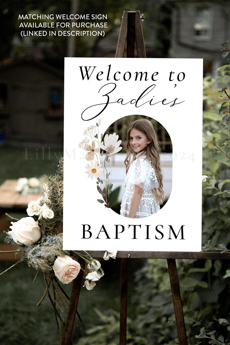 May include: White welcome sign with a floral design and a photo of a girl. The sign says "Welcome to Zadies Baptism".