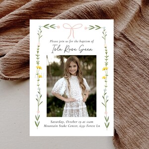 May include: A white card with a floral border and a pink ribbon. The text reads "Please join us for the baptism of Isla Rose Green. Saturday, October 19 at 11am Mountain Stake Center, 6331 Forest Ln."