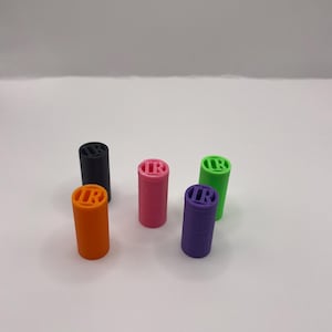 May include: A collection of six cylindrical objects in various colors: orange, black, pink, purple, and green. Each cylinder has the letters "IR" on the top. The objects are arranged on a white surface.