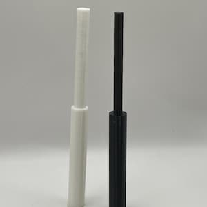 Puede incluir: Dos objetos cilíndricos verticales, uno blanco y otro negro. Ambos tienen una base ligeramente más ancha y un acabado liso y mate. El objeto blanco está a la izquierda y el negro a la derecha. El fondo es gris claro liso.