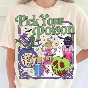 May include: A cream-colored t-shirt featuring a graphic with the text Pick Your Poison. The design includes a purple pot labeled Deadly Night Shade, a pink potion bottle, a blue bottle with a Poison tag, and a green skull-shaped apple.