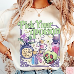 May include: Cream-colored t-shirt with a whimsical design featuring the text "Pick Your Poison" in green. The graphic includes potion bottles, a skull, and a cauldron with the words "Deadly Nightshade".