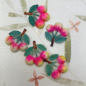May include: Four clusters of decorative cherries. Each cluster has pink and yellow fruit with green leaves and brown stems. The cherries are arranged on a white background with a floral pattern.