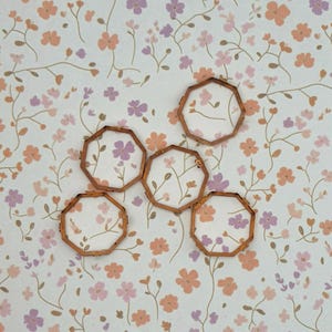 May include: Five small, empty, octagonal metal frames with a thin, metallic copper-toned finish. Each frame features a simple, geometric eight-sided shape with a hollow centre, arranged in a scattered pattern across the visual field.