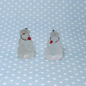 May include: Two small, frosted glass dog figurines. Each dog has a red nose, a silver wire collar, and a small gold-colored detail on its head. The background is a light blue surface with white polka dots.