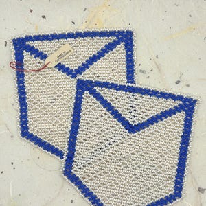 May include: Two beaded coasters with a white background and a blue border. The coasters are shaped like envelopes. A tag attached to one coaster reads "MADE IN CZECHOSLOVAKIA".