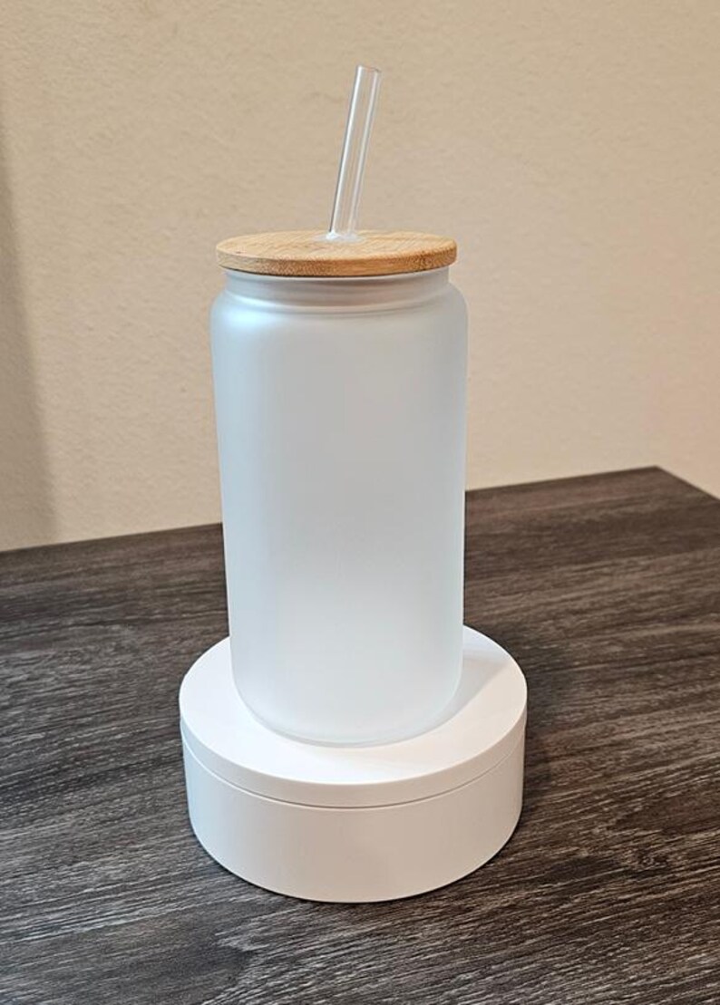 Puede incluir: Un vaso de vidrio esmerilado con tapa de bamb&uacute; y una pajita transparente. El vaso est&aacute; sobre un pedestal blanco.