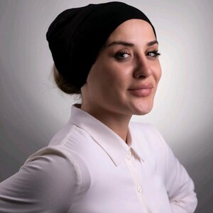 May include: A black head covering, possibly a beanie or cap, is worn. The person is wearing a white collared shirt. The background is a gradient of grey.