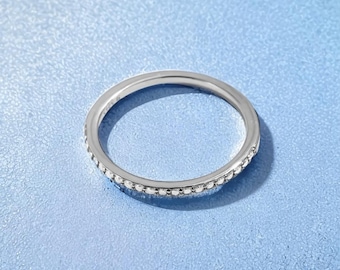 May include: A thin silver band ring with a row of small clear stones around the edge.