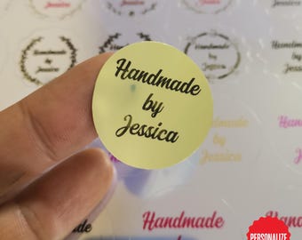 May include: A close-up of a round, pale yellow sticker with the words "Handmade by Jessica" in black script. Other similar stickers are visible in the background, some with floral designs.