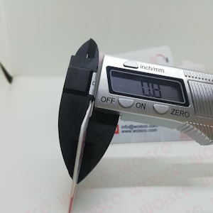 May include: A digital caliper measuring a thin object. The display reads 0.8 inches. The caliper is silver with black measuring jaws. The background includes a white surface and a business card.