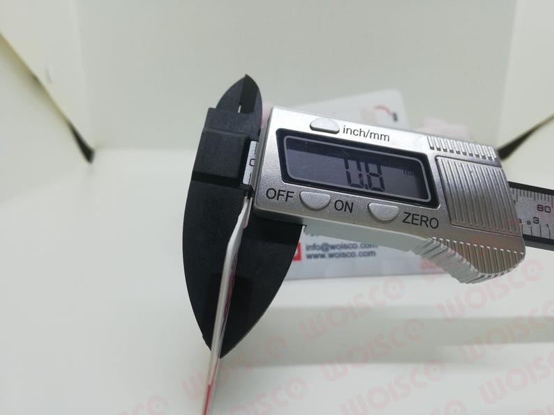 May include: A digital caliper measuring a thin object. The display reads 0.8 inches. The caliper is silver with black measuring jaws. The background includes a white surface and a business card.