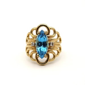 May include: A gold ring with a blue topaz marquise-shaped gemstone and two smaller diamonds. The ring has a delicate, intricate design.